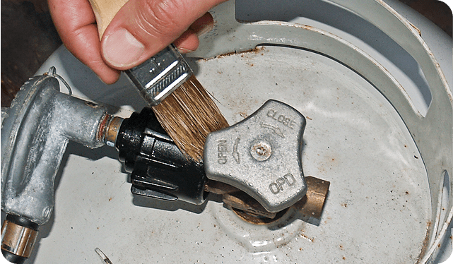 Hand applying leak detector solution to propane cylinder valve